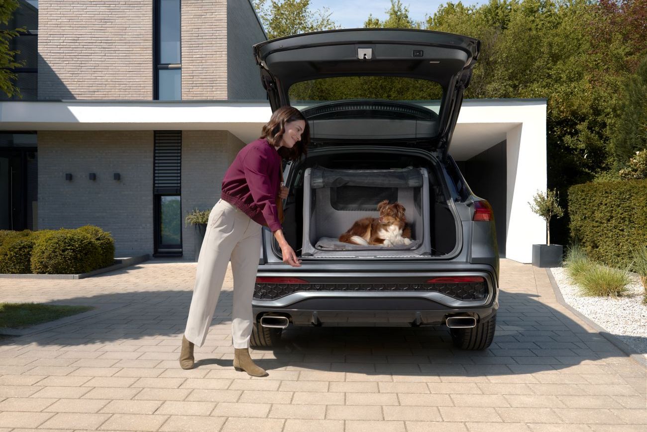 Eine Frau lächelt ihrem Hund, der in der Audi Hundebox im geöffneten Kofferraum eines Audi Q5 liegt, zu.