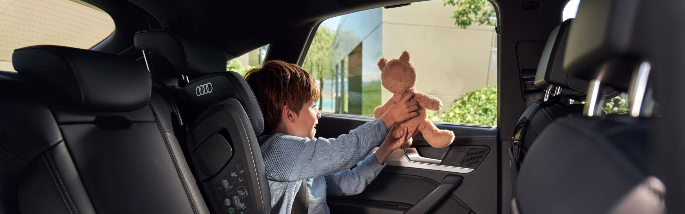 Ein Junge im Kindersitz mit Teddybär auf dem Rücksitz eines Audi.