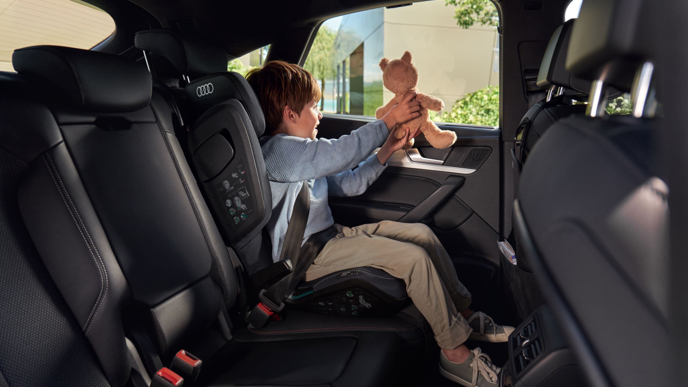 Ein Junge im Kindersitz mit Teddybär auf dem Rücksitz eines Audi.