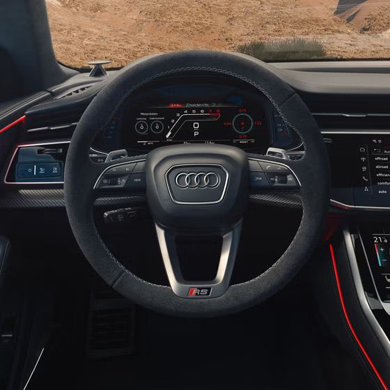 Blick von hinten auf das Cockpit des RS Q8 SUV mit Fokus auf das Lenkrad und die digitalen Displays. Durch die Windschutzscheibe sind karge Felsen zu erkennen.