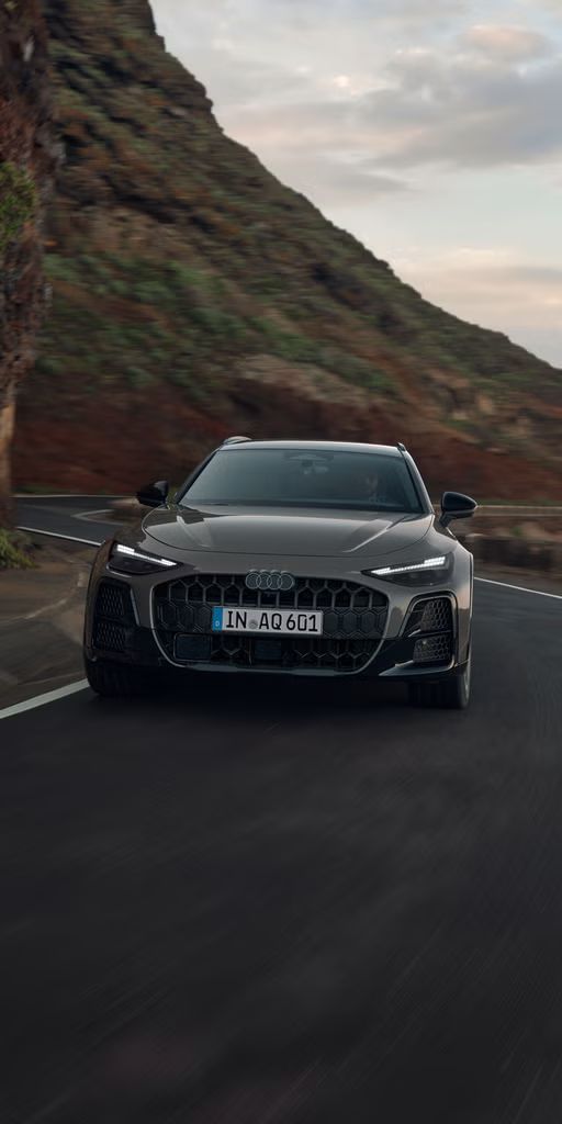 Der Audi A6 allroad von vorn auf durchfährt eine kurvige Gebirgsstraße. Links ragen steile Felswände auf.