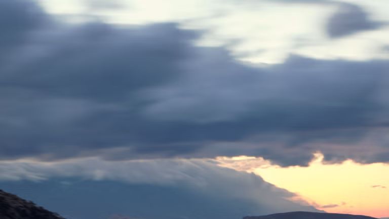 Der Q4 SUV e-tron von hinten bei Nacht auf einer abschüssigen Gebirgstraße, zur rechten das Meer. Auf der Gegenfahrbahn sind Lichtschleier entgegenkommender Fahrzeuge zu sehen. 