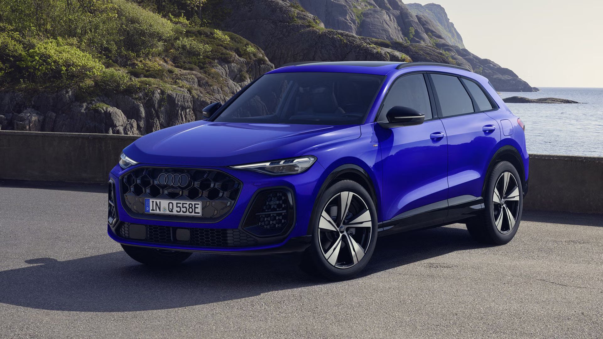 Ein Q5 SUV e-hybrid mit der Individuallackierung Nogaroblau Perleffekt steht im schrägen Frontprofil an einer felsigen Küste.