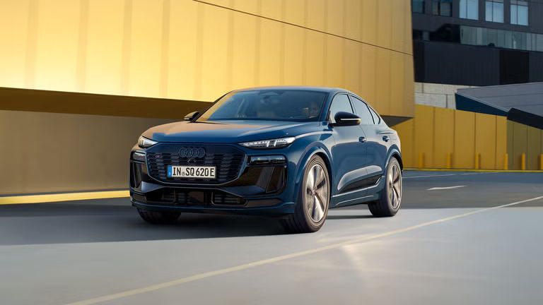 Ein blauer Audi SQ6 Sportback e-tron fährt auf einer Straße vor einem gelben Gebäude.
