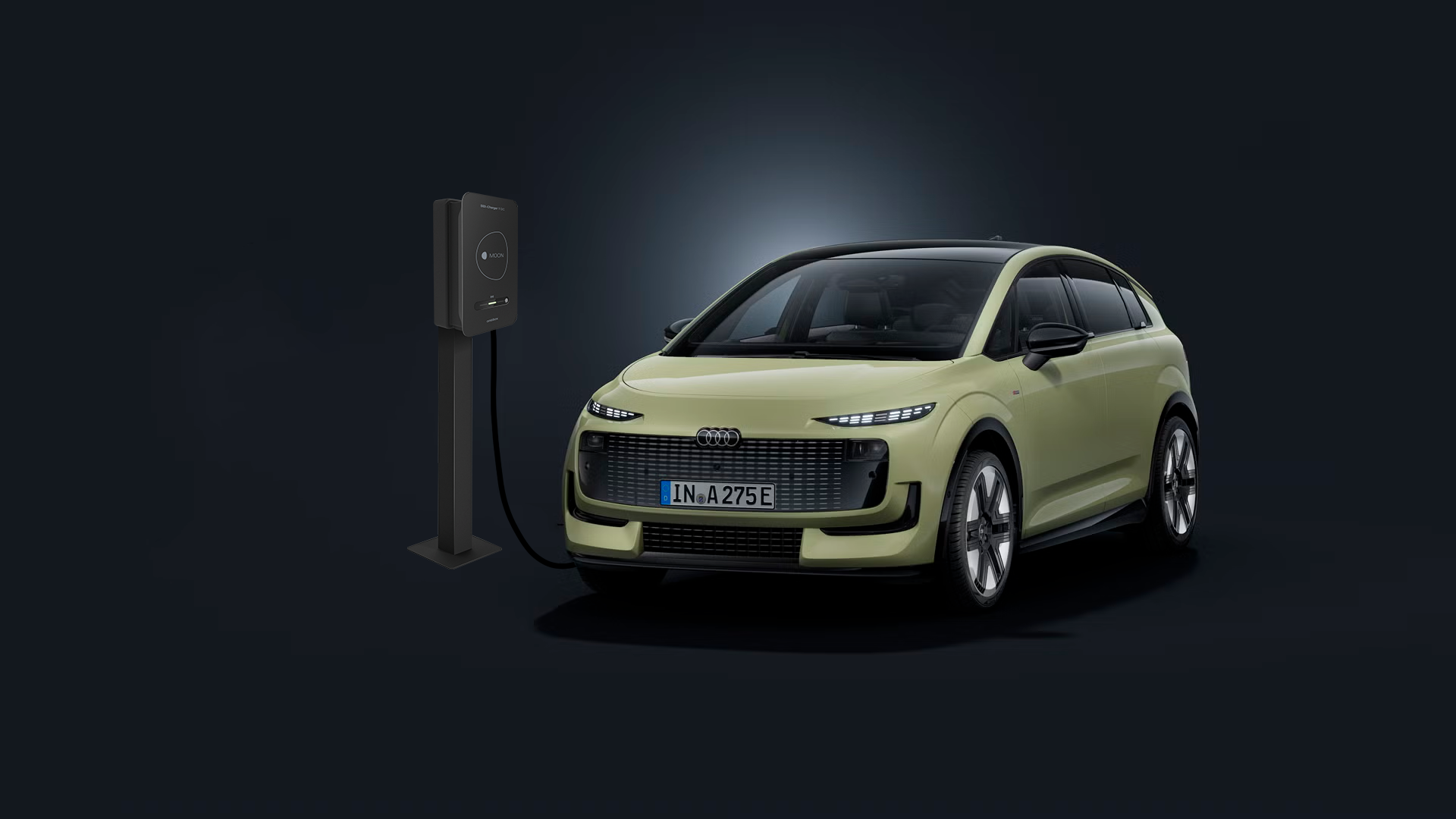 Der Audi A2 e-tron schräg von vorn auf dunklem Hintergrund, links dahinter eine Ladesäule.