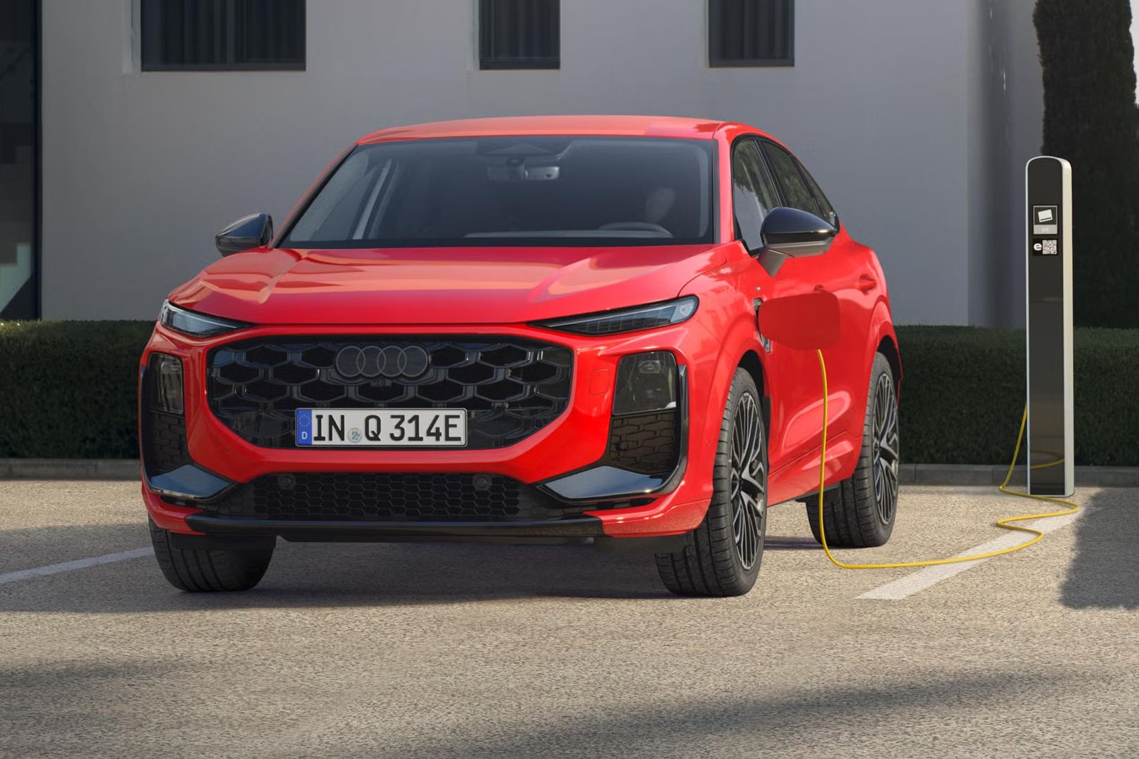 Ein roter Q3 Sportback e-hybrid parkt vor einer Ladesäule und wird mit Strom betankt.	