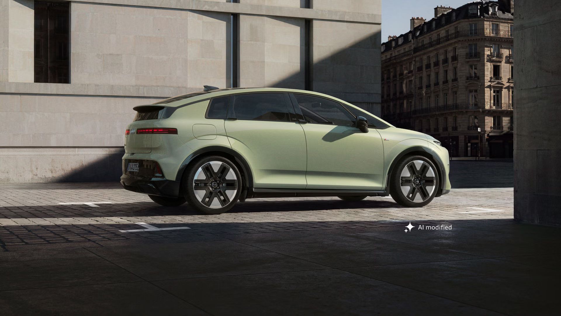 Der Audi A2 e-tron, fotografiert von der Seite, parkt vor einem modernen Gebäude in urbaner Umgebung. Das schräg einfallende Sonnenlicht taucht die Szenerie teilweise in Schatten.