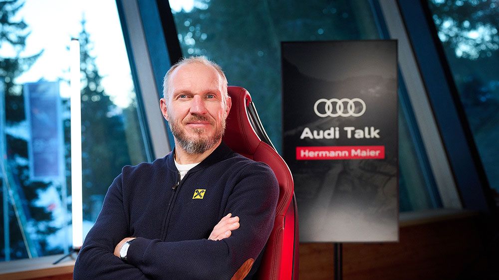 Hermann Maier sitzt auf einem roten Stuhl. Im Hintergrund ist ein Bildschirm mit der Aufschrift "Audi Talk Hermann Maier". 