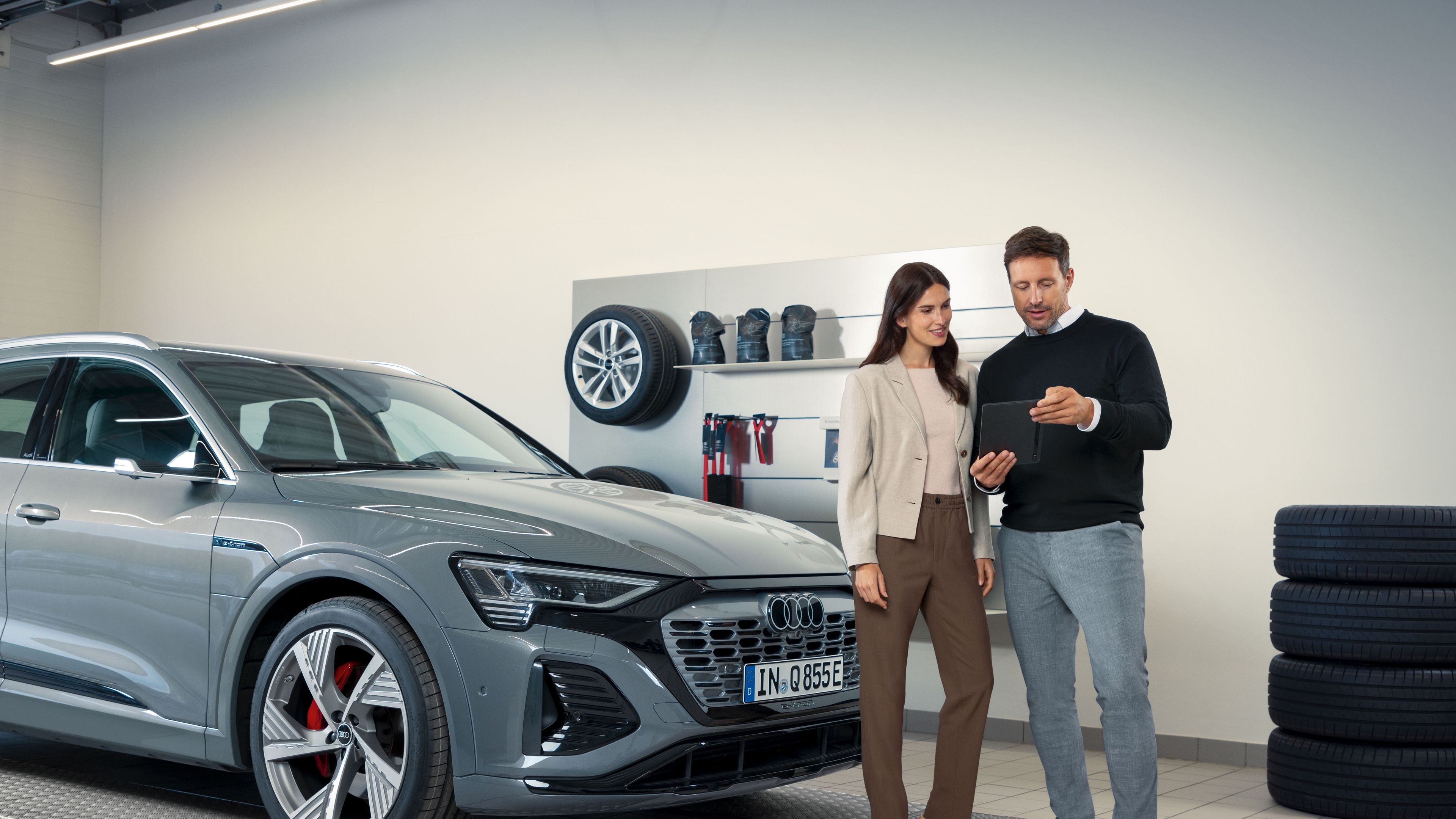 Ein Audi Service Mitarbeiter im Gespräch mit einer Kundin, beide stehen vor einem Audi Elektroauto