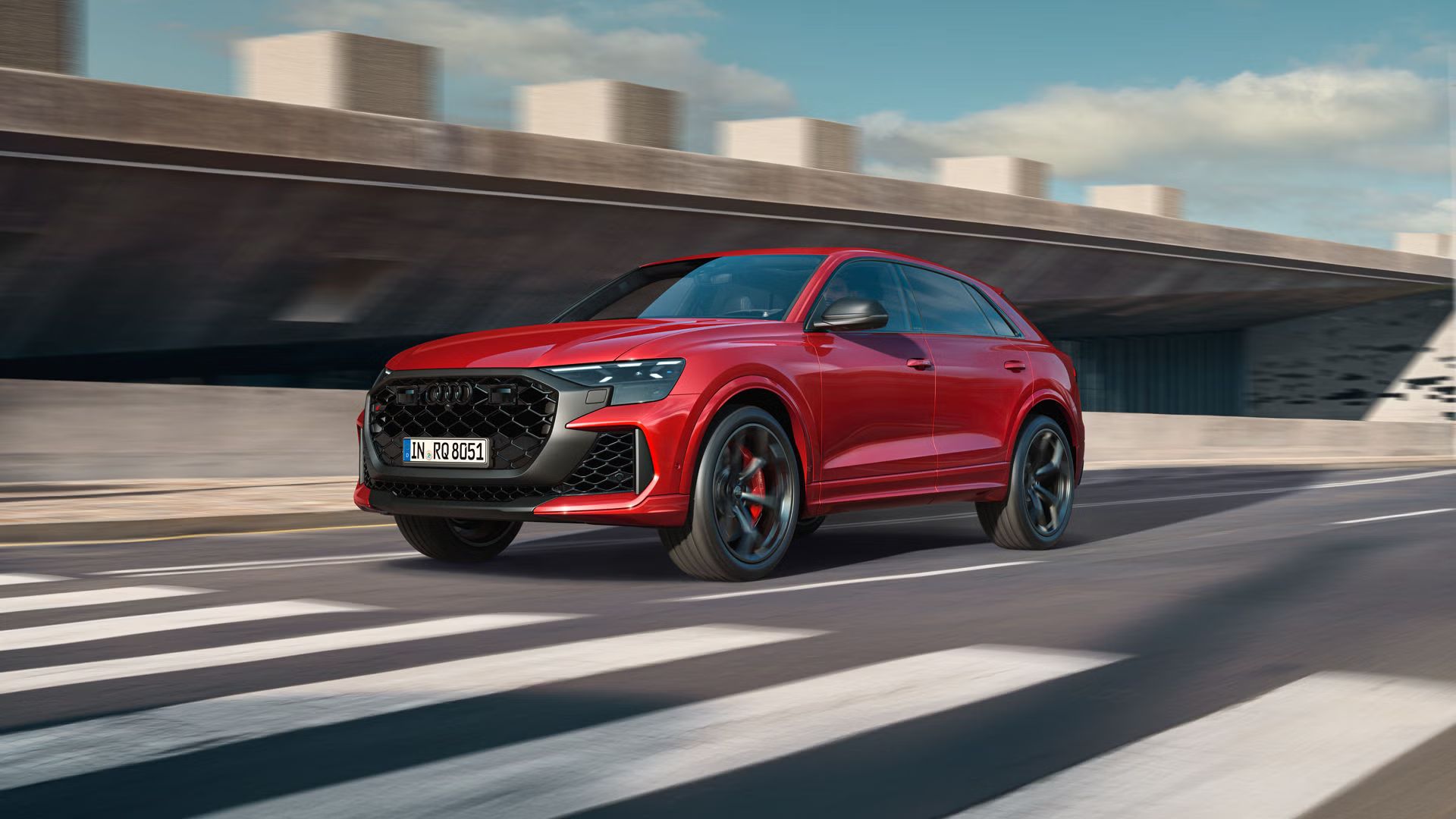 Der RS Q8 SUV performance schräg von vorn nähert sich einem Zebrastreifen. Rechts daneben ein futuristisches Gebäude in Betonoptik.