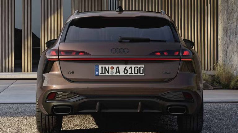 Heckaufnahme des A6 Avant, der auf einer Kiesfläche vor einer Fassade mit Holzvertäfelung und hohen Fenstern steht.