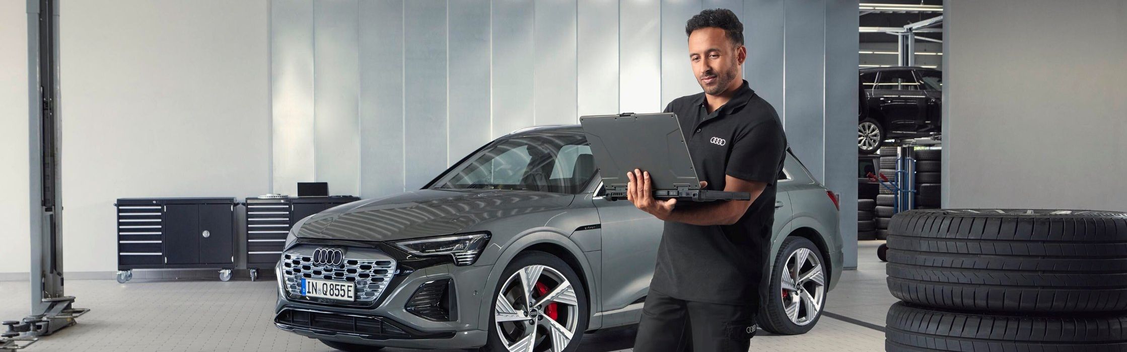 Ein Audi Service Mitarbeiter steht neben gestapelten Reifen und blickt auf sein Notebook.