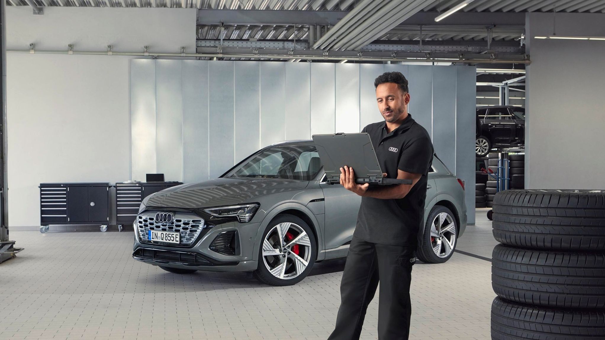 Ein Audi Service Mitarbeiter steht neben gestapelten Reifen und blickt auf sein Notebook.
