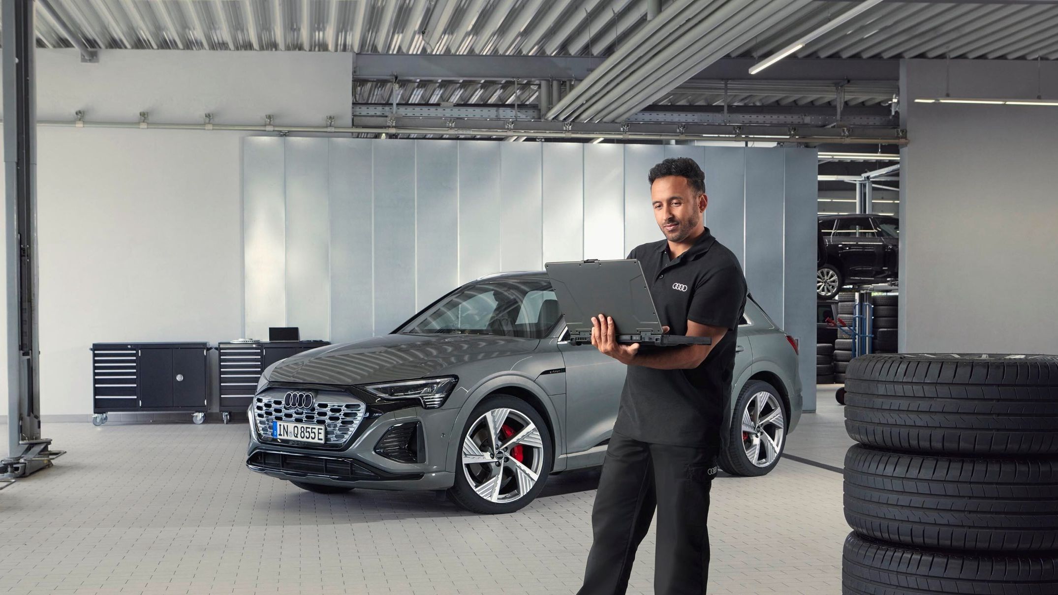 Ein Audi Service Mitarbeiter steht neben gestapelten Reifen und blickt auf sein Notebook.