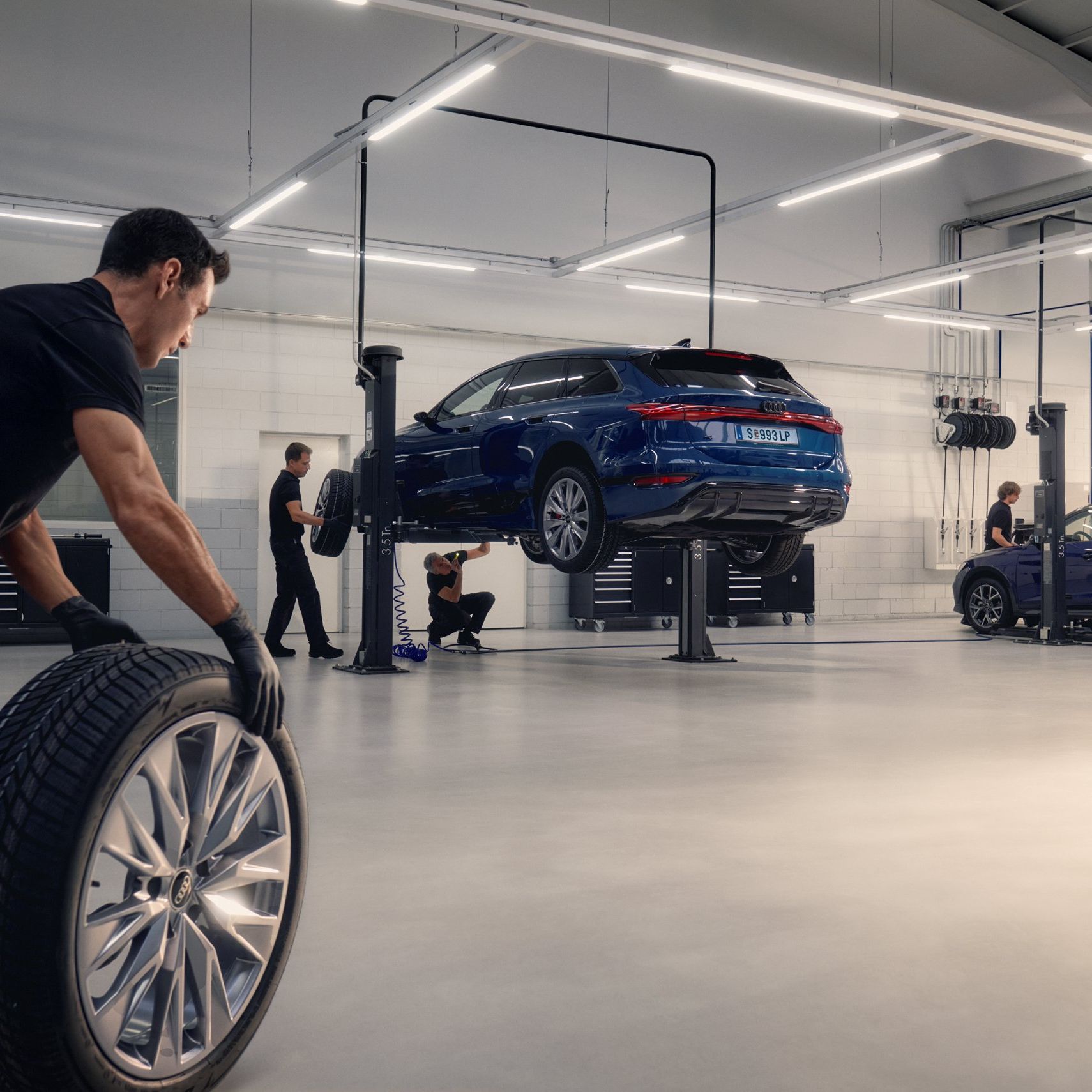 Ein Audi Mechaniker rollt ein Winterkomplettrad in Richtung eines Audi auf einer Hebebühne.