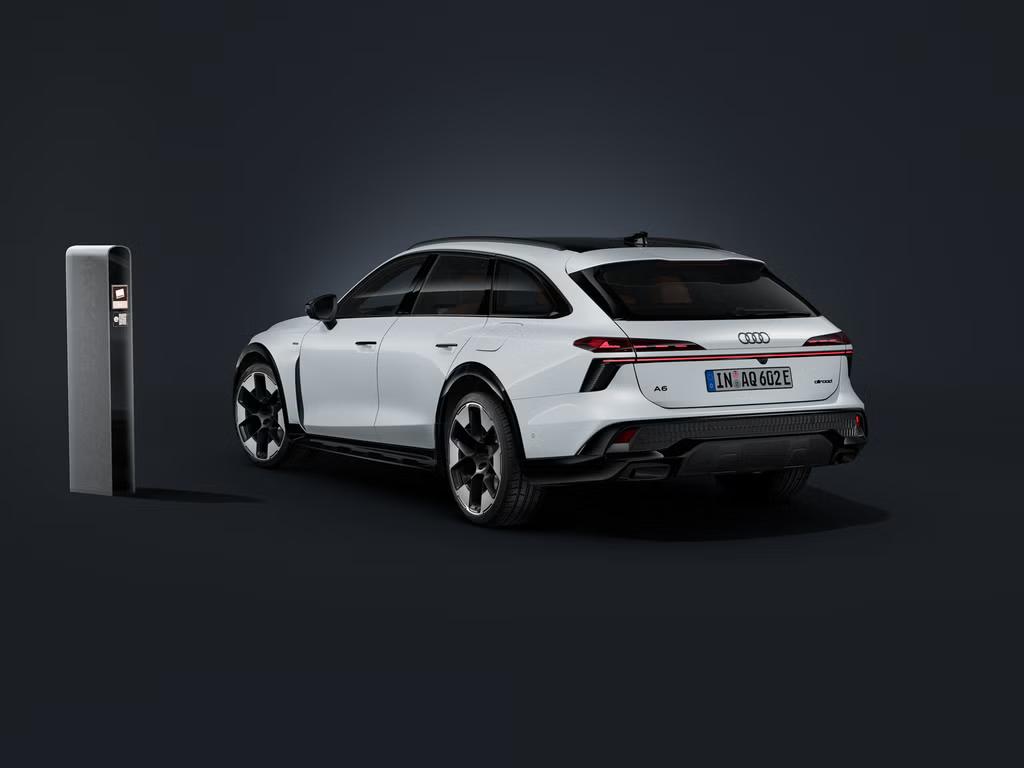 Der Audi A6 allroad e-hybrid schräg von hinten auf dunklem Hintergrund. Daneben eine moderne Ladesäule.