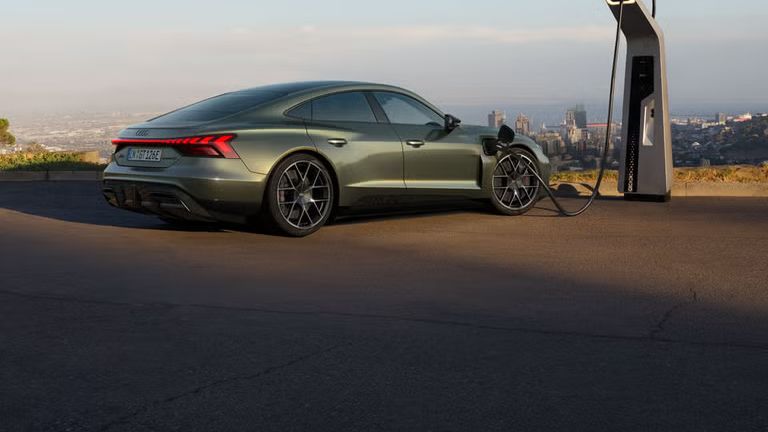 Grüner Audi RS e-tron GT performance lädt an einer Schnellladestation mit Stadtblick im Hintergrund.