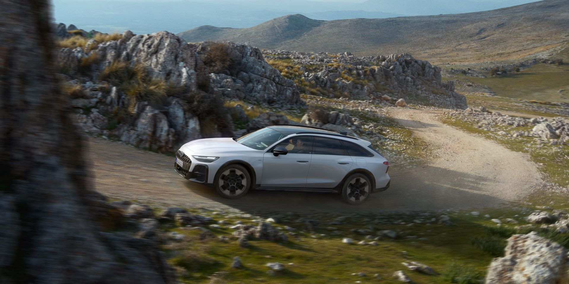 Der Audi A6 allroad e-hybrid durchquert eine steile Schotterstraße in felsiger Umgebung.