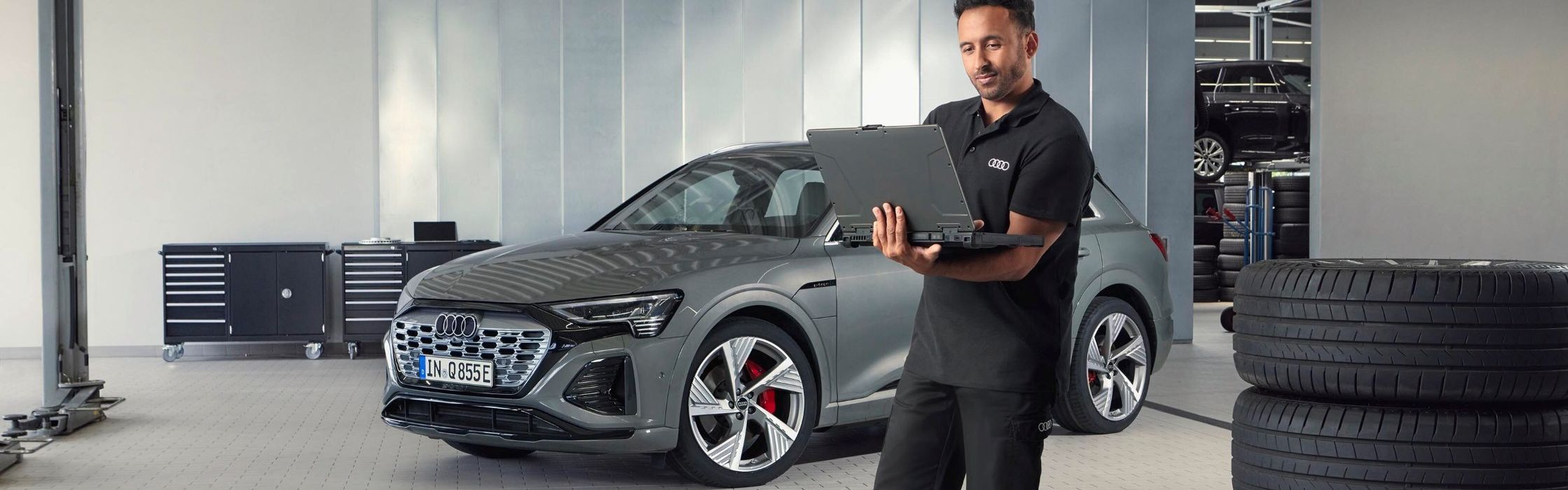 Ein Audi Service Mitarbeiter steht neben gestapelten Reifen und blickt auf sein Notebook.