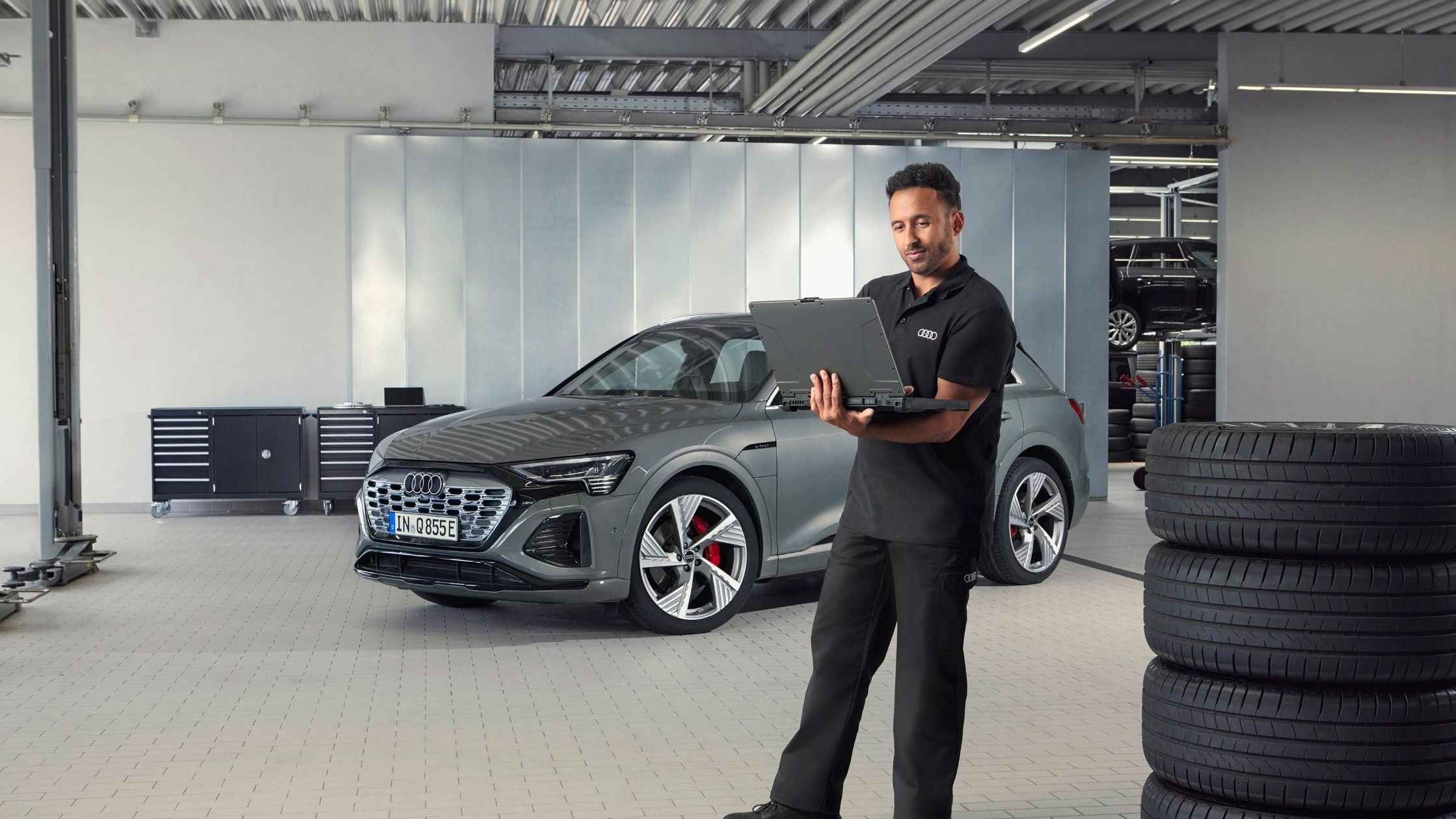 Ein Audi Service Mitarbeiter steht neben gestapelten Reifen und blickt auf sein Notebook.