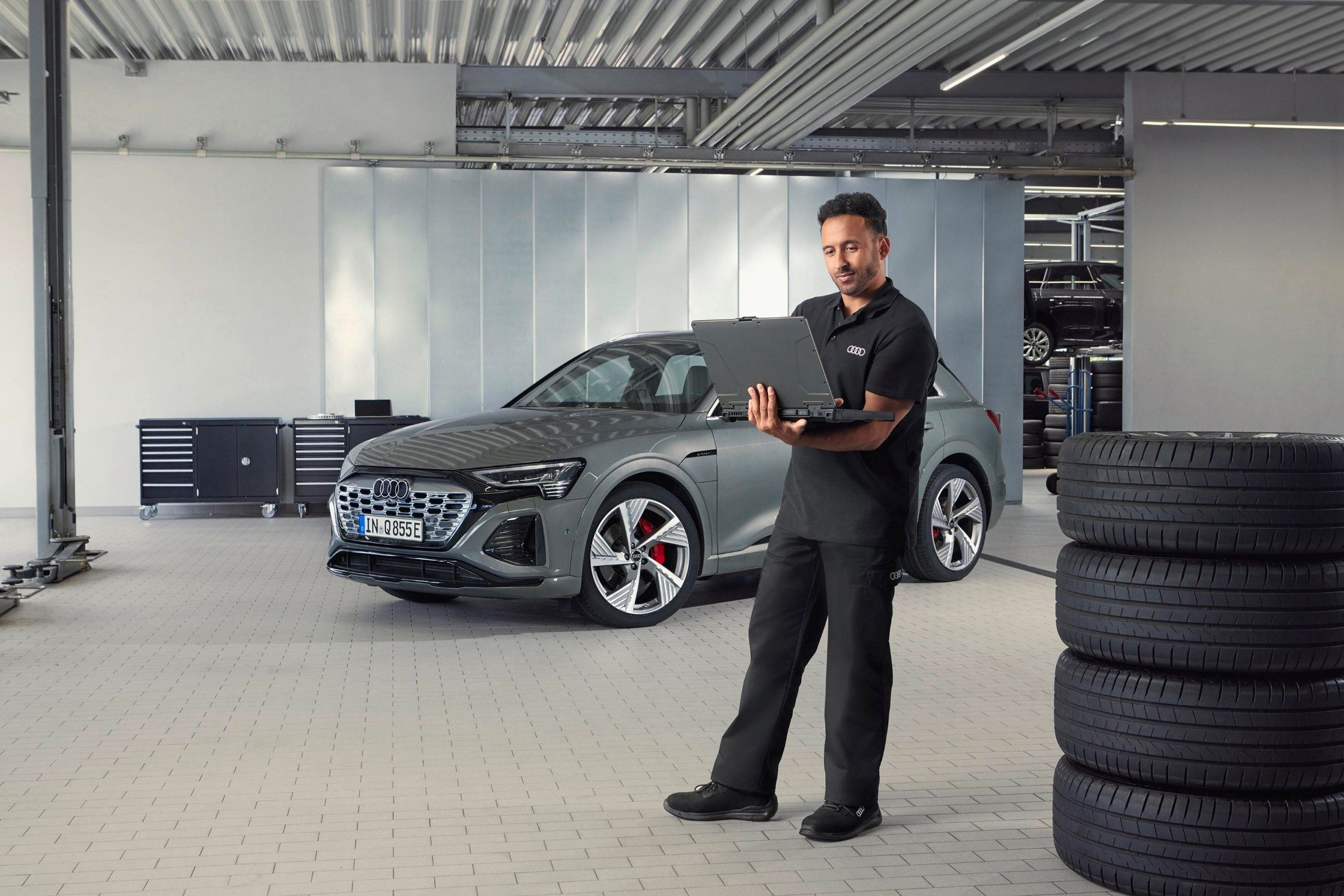Ein Audi Service Mitarbeiter steht neben gestapelten Reifen und blickt auf sein Notebook.