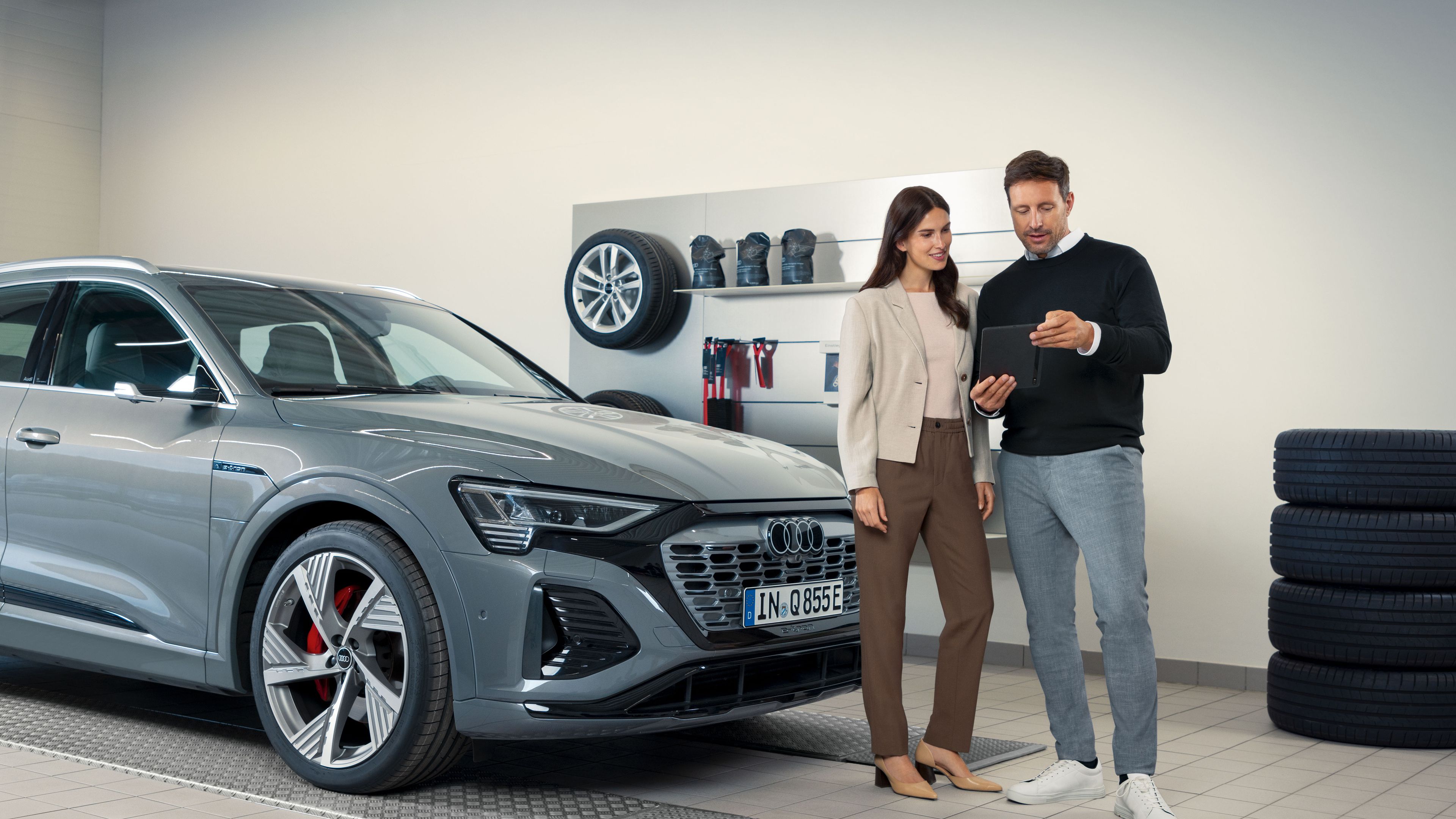 Ein Audi Service Mitarbeiter im Gespräch mit einer Kundin, beide stehen vor einem Audi Elektroauto