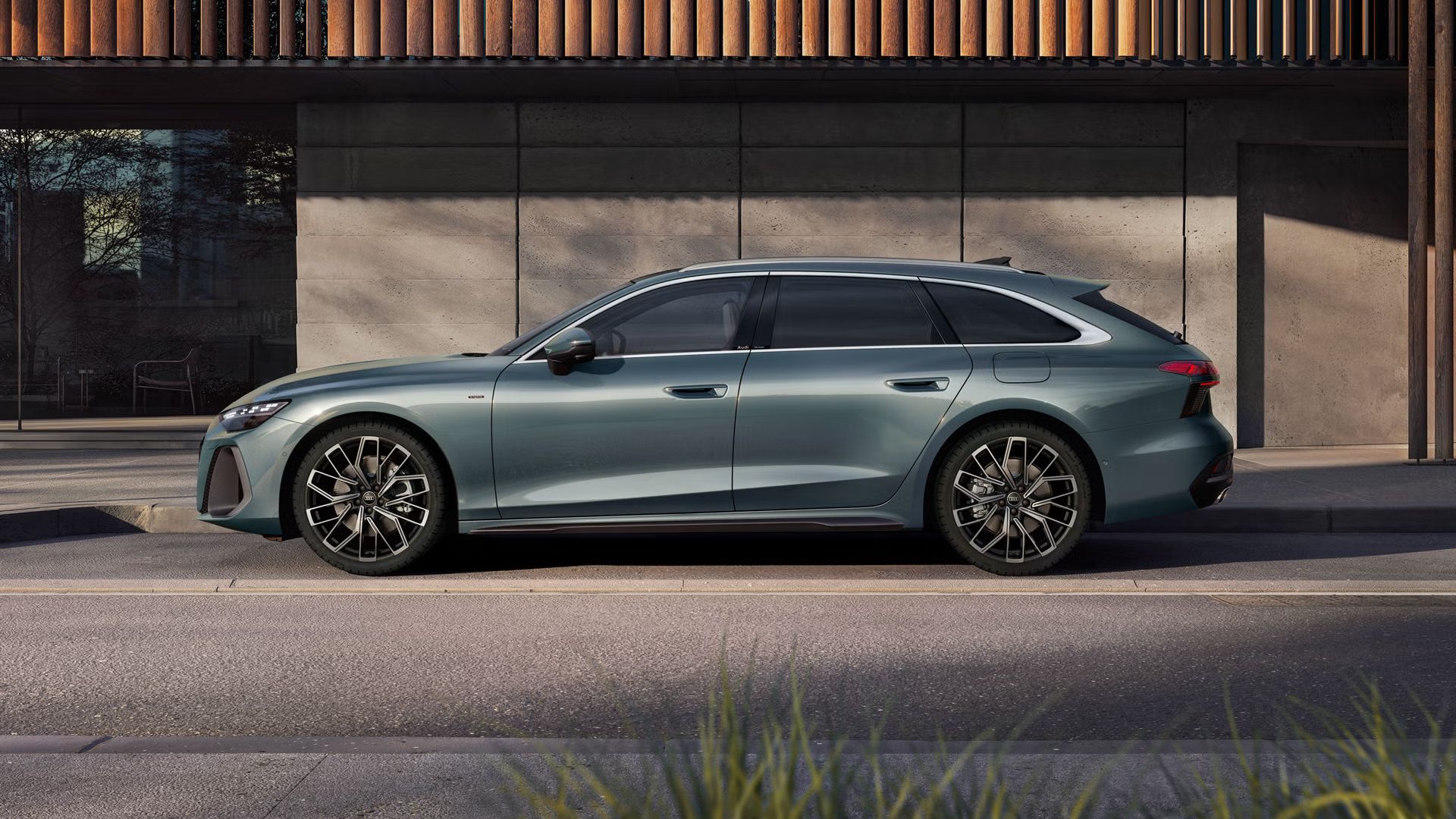 Der A6 Avant e-hybrid in Morgentaugrün steht im Seitenprofil vor der Fassade eines Gebäudes.