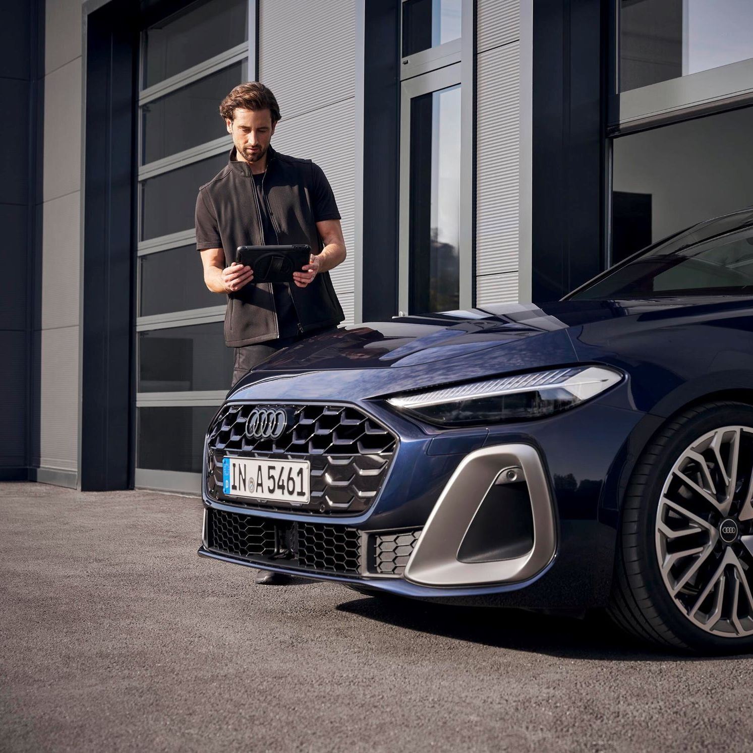 Ein Audi Service Techniker steht vor einem Audi und blickt auf sein Tablet
