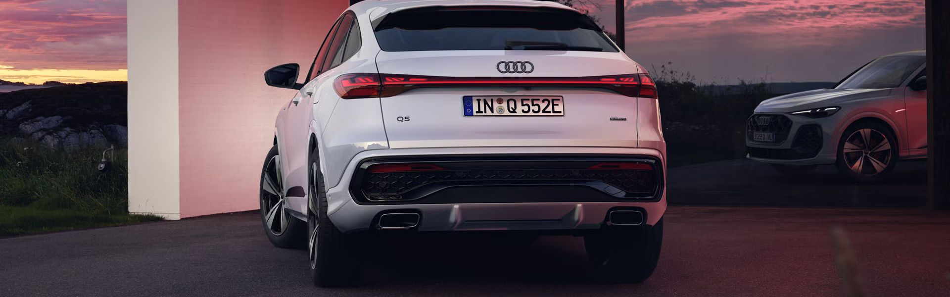 Heckansicht des Q5 Sportback e-hybrid, welcher vor bodentiefen Fenstern eines Hauses steht und diese mit seinen Scheinwerfern anleuchtet.