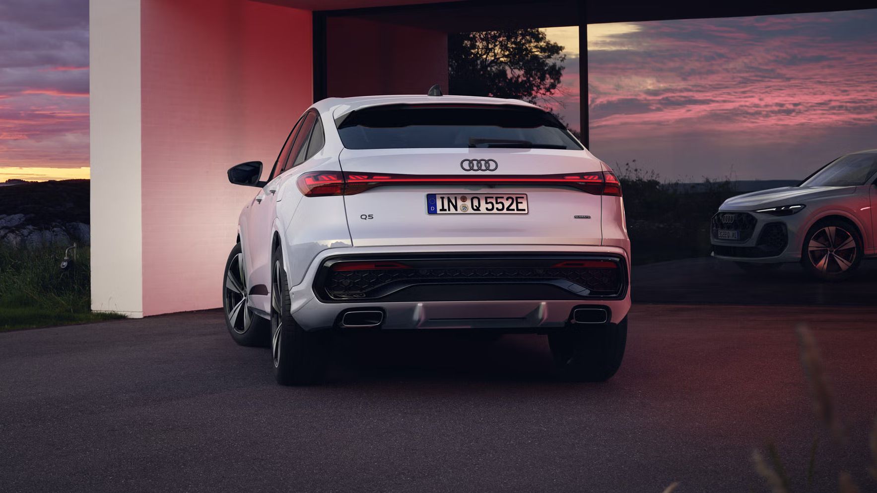 Heckansicht des Q5 Sportback e-hybrid, welcher vor bodentiefen Fenstern eines Hauses steht und diese mit seinen Scheinwerfern anleuchtet.