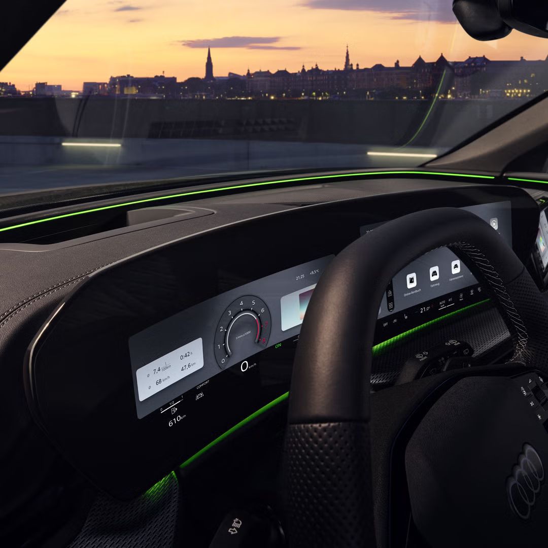Blick durch das Fahrerfenster in das Cockpit des SQ5 SUV. Zu sehen sind das Audi virtual Cockpit, sowie das Interaktionslicht am unteren Rand der Windschutzscheibe. Durch die Scheibe ist eine Stadt bei Sonnenuntergang zu sehen.