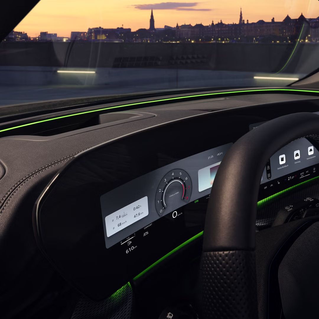 Blick durch das Fahrerfenster in das Cockpit des SQ5 SUV. Zu sehen sind das Audi virtual Cockpit, sowie das Interaktionslicht am unteren Rand der Windschutzscheibe. Durch die Scheibe ist eine Stadt bei Sonnenuntergang zu sehen.