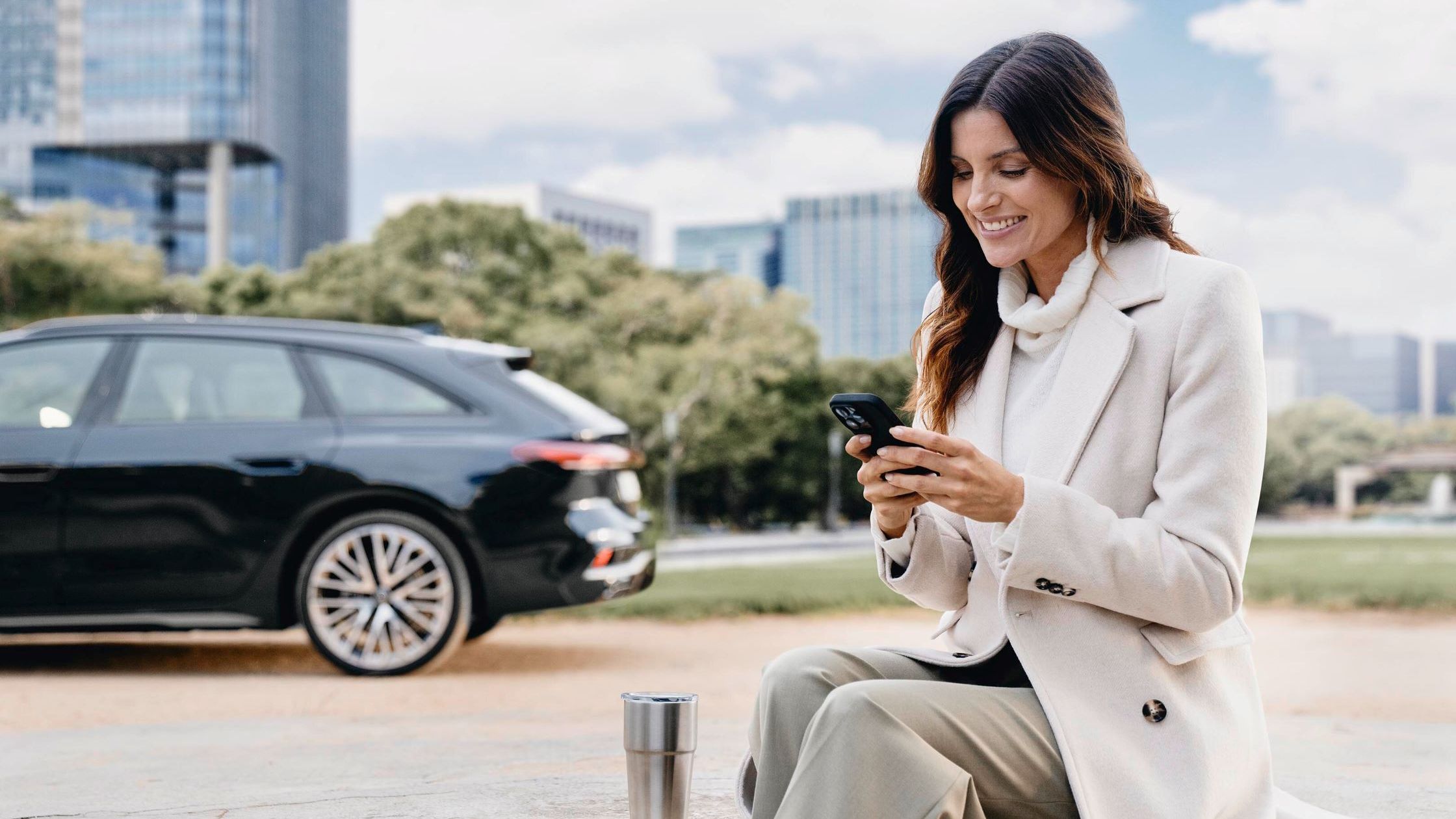 Eine Frau blickt auf ihr Smartphone, im Hintergrund ist ein Audi zu sehen.