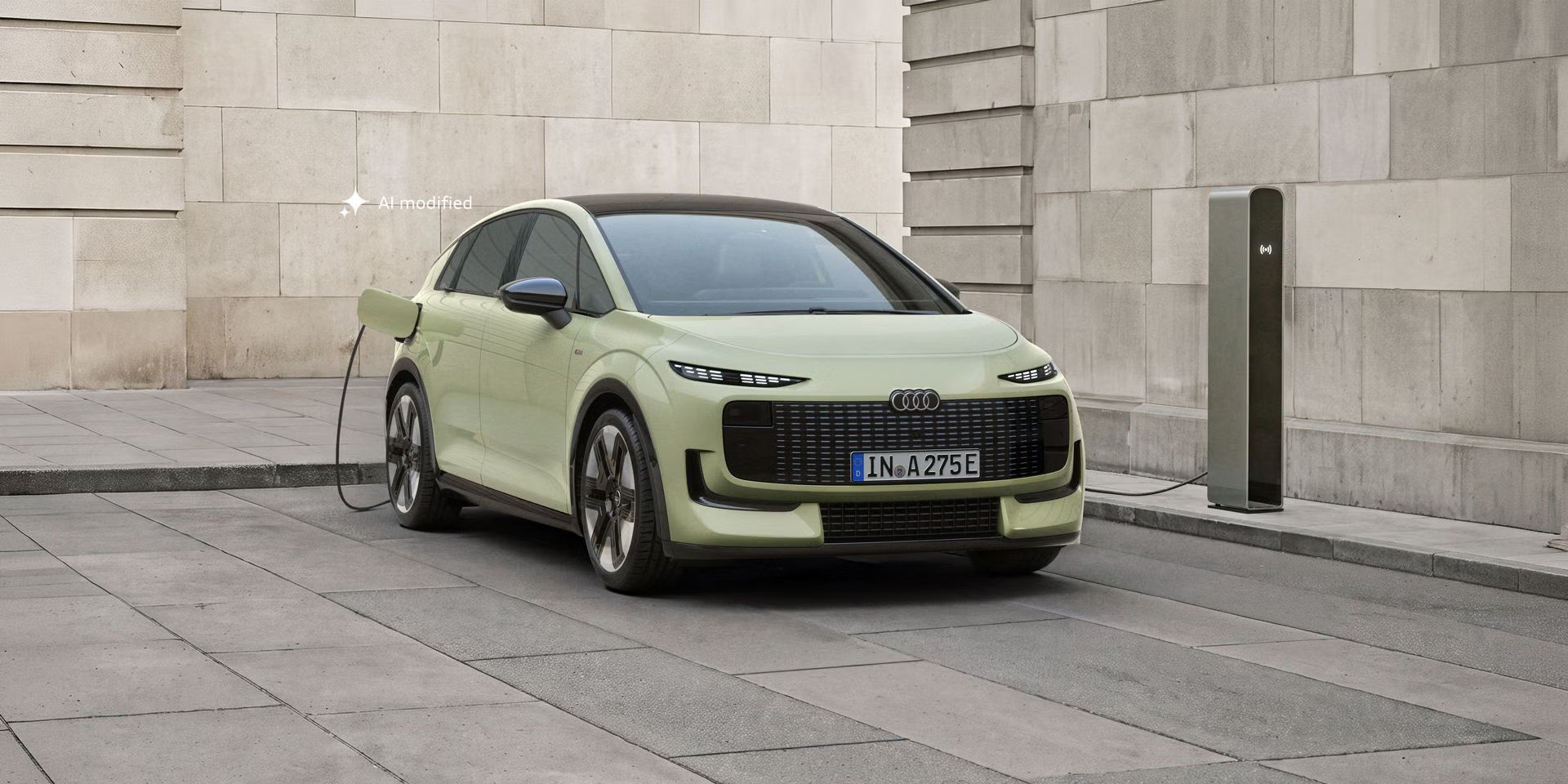 Der Audi A2 e-tron, frontal von hinten fotografiert, parkt vor einem modernen Gebäude. Das Fahrzeug ist an eine Ladesäule angeschlossen.
