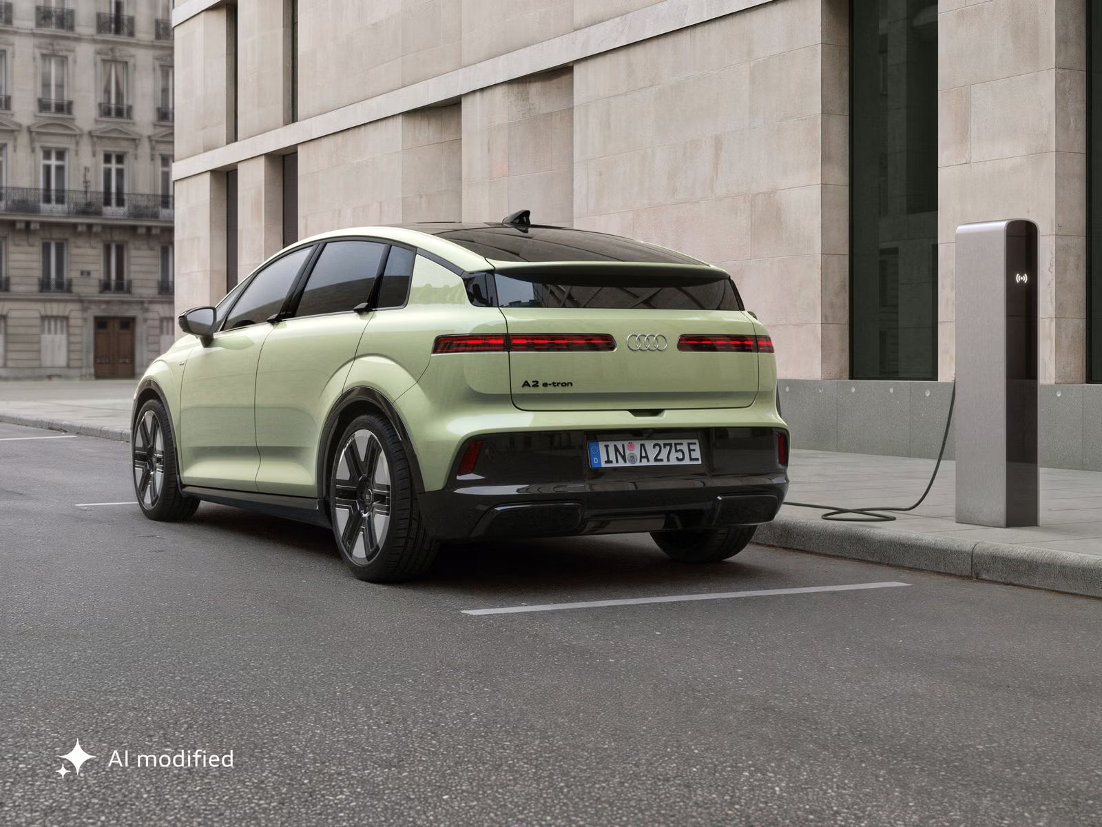 Der Audi A2 e-tron, schräg von hinten fotografiert, parkt vor einem modernen Gebäude. Das Fahrzeug ist an eine Ladesäule angeschlossen.