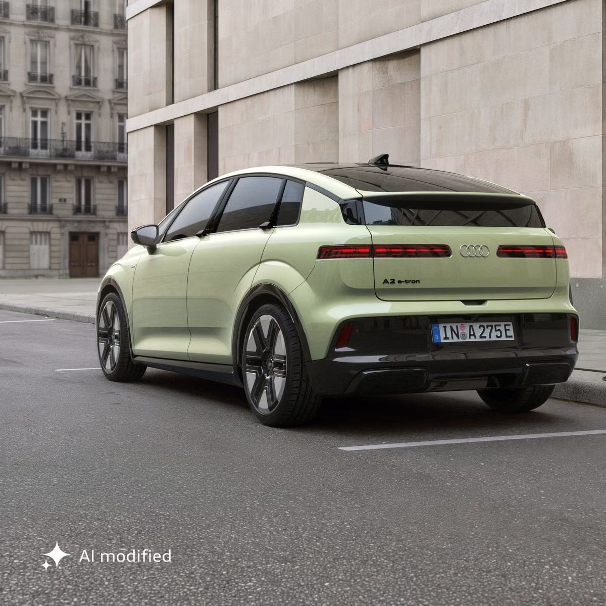 Der Audi A2 e-tron, schräg von hinten fotografiert, parkt vor einem modernen Gebäude. Das Fahrzeug ist an eine Ladesäule angeschlossen.