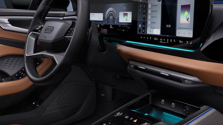 Blick von der Beifahrerseite des Audi A6 allroad e-hybrid auf das Cockpit mit Lenkrad, Mittelkonsole, digitale Displays und das Ambiente-Licht.
