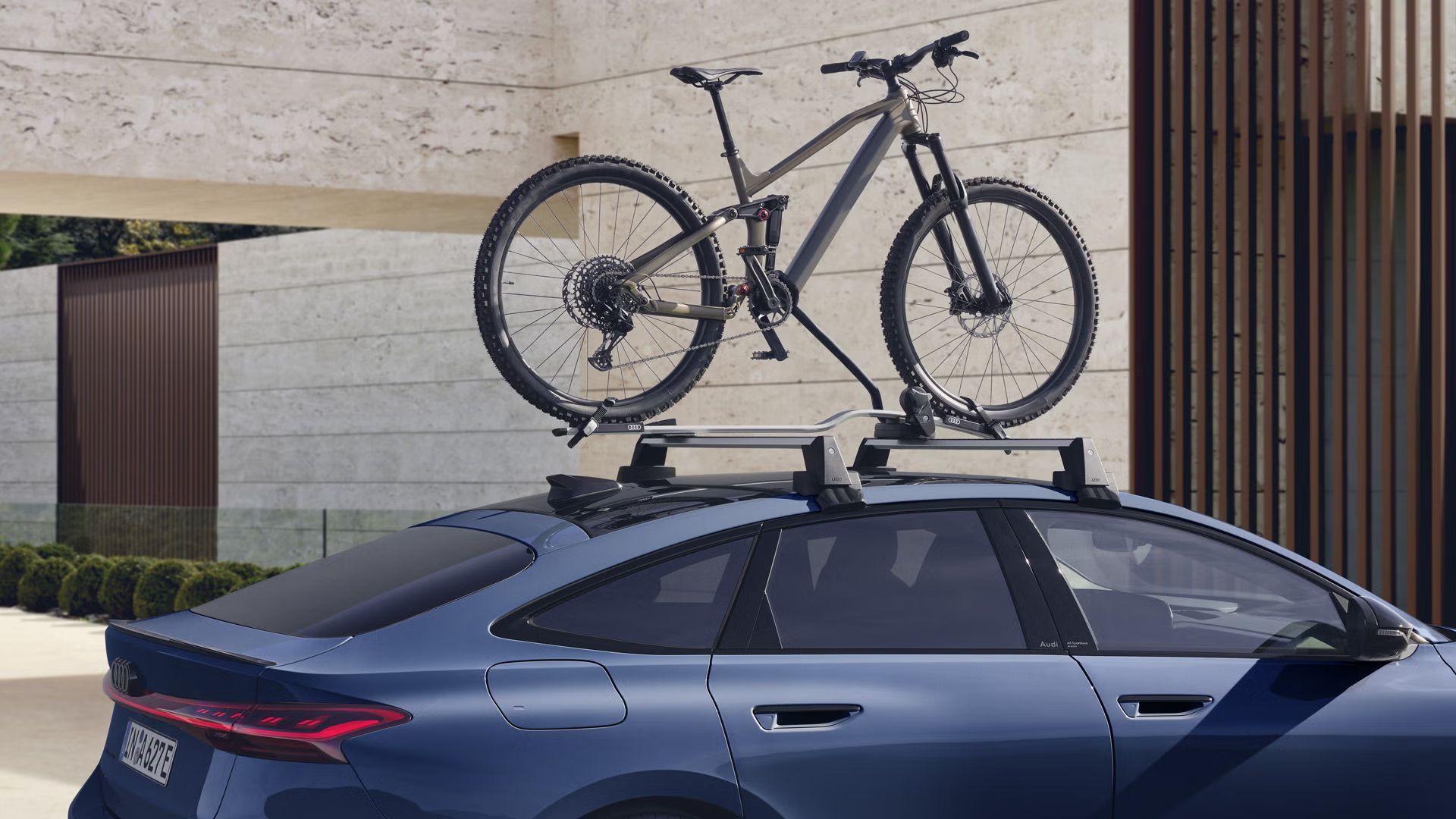 Der A6 Sportback e-tron im Anschnitt vor einem modernen Haus. Auf dem Dachgepäckträger ist ein Mountain Bike festgezurrrt. 