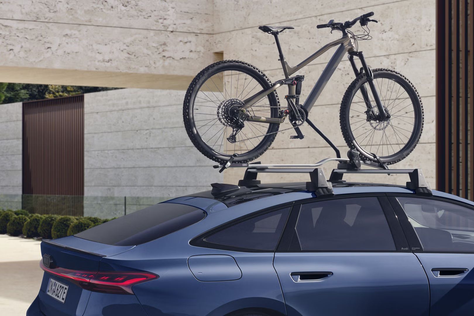Der A6 Sportback e-tron im Anschnitt vor einem modernen Haus. Auf dem Dachgepäckträger ist ein Mountain Bike festgezurrrt. 
