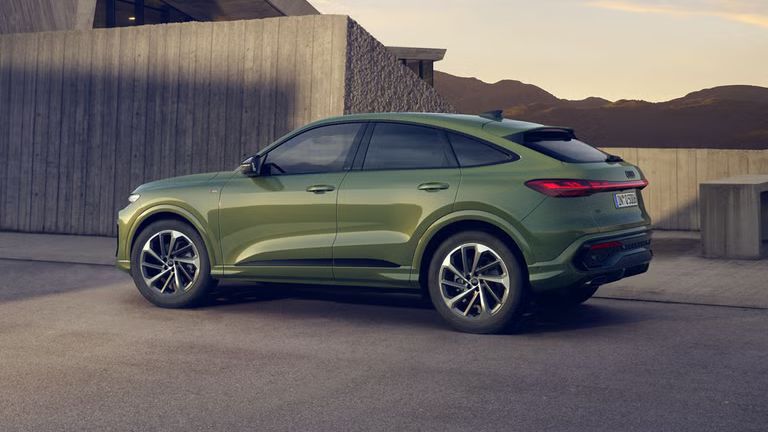 Ein grüner Q5 Sportback in Seitenansicht steht auf einem Parkplatz vor einem urbanen Haus in bergiger Umgebung.
