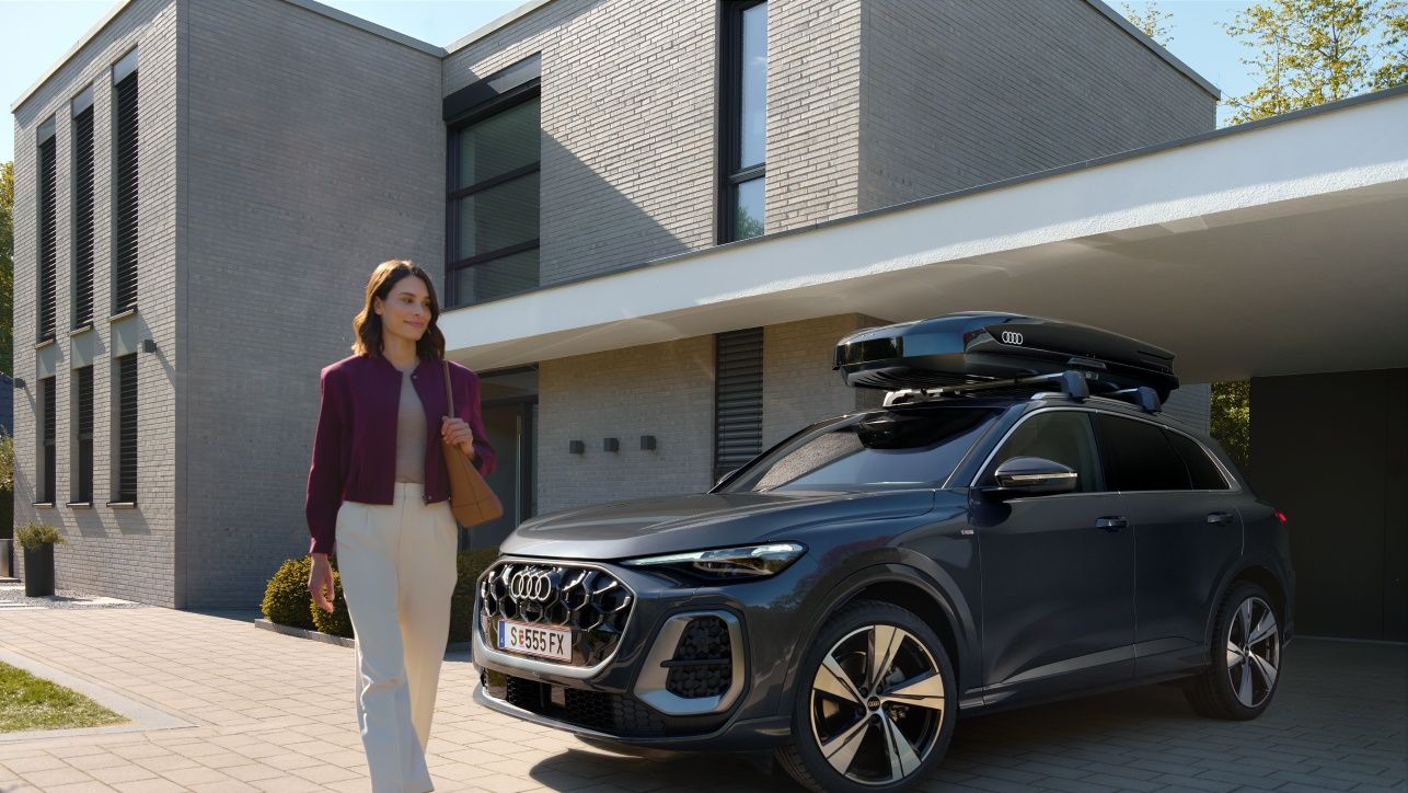 Frau passiert lächelnd einen in der Hauseinfahrt parkenden Audi Q5 mit Dachbox