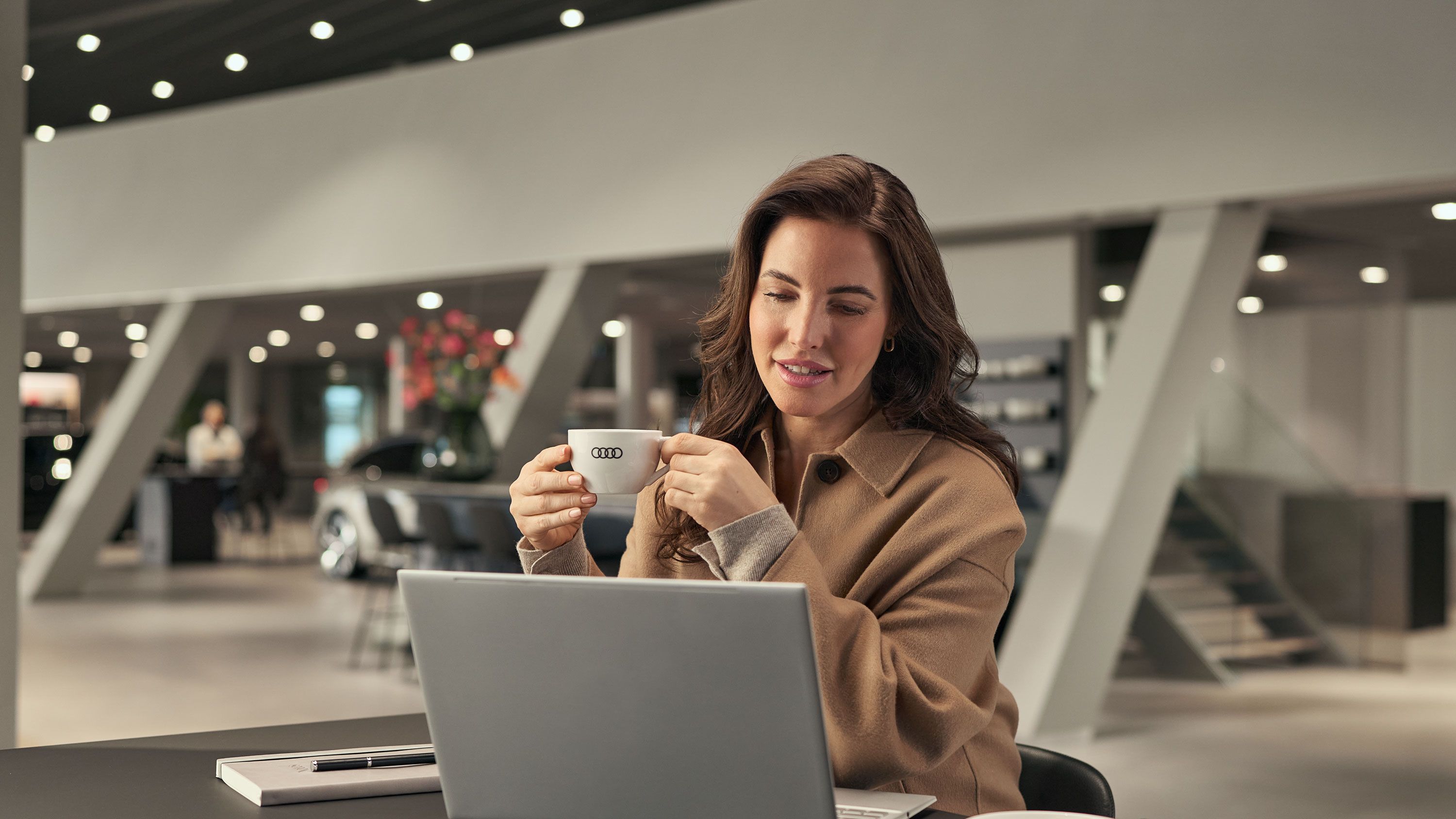 Ein Kunde arbeitet in der Working Lounge an seinem Laptop und genießt dabei einen Kaffee; Notizbuch und Stift liegen auf dem Tisch.
