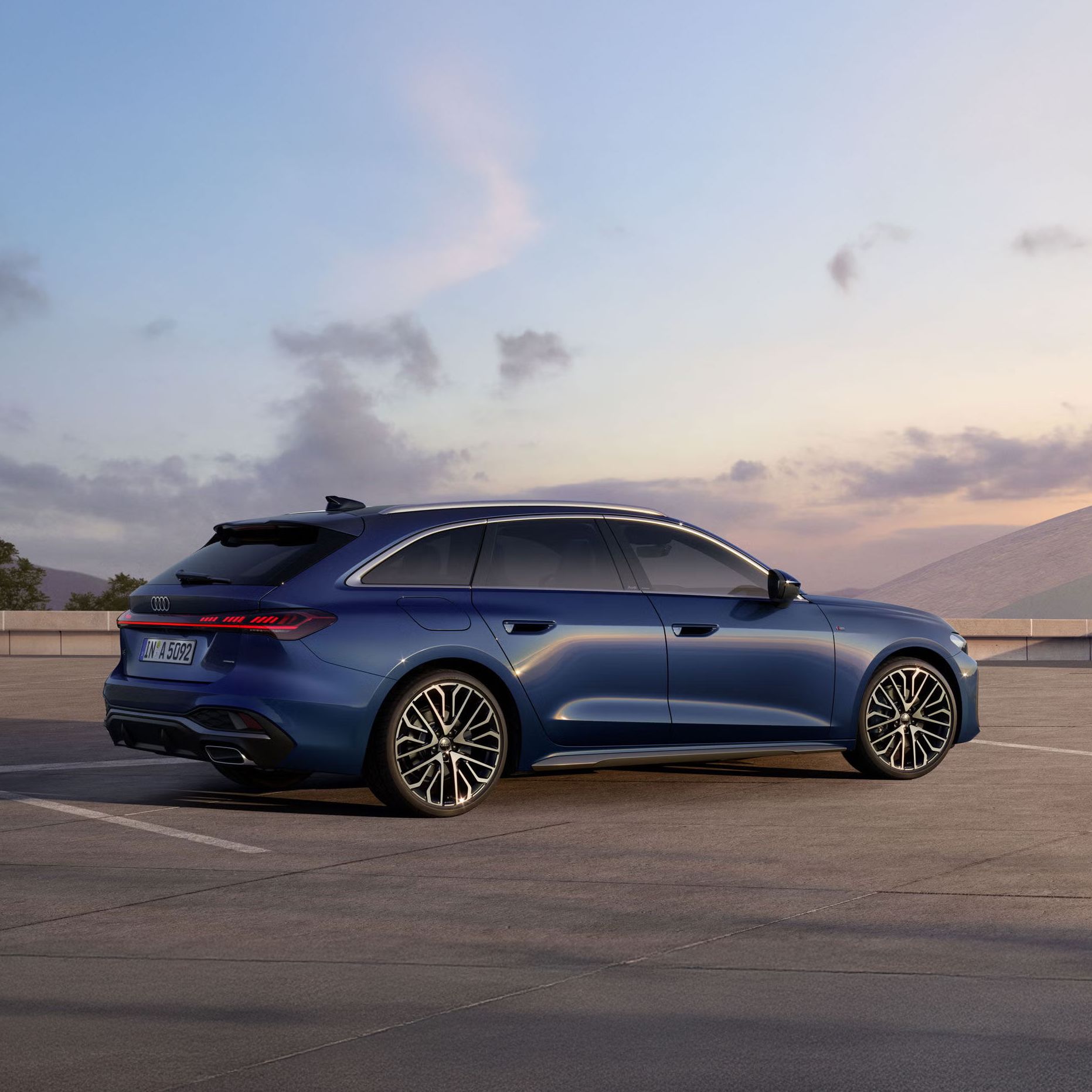Der A5 Avant in Ascariblau Metallic steht im schrägen Seitenprofil auf einem großen Parkplatz. 
