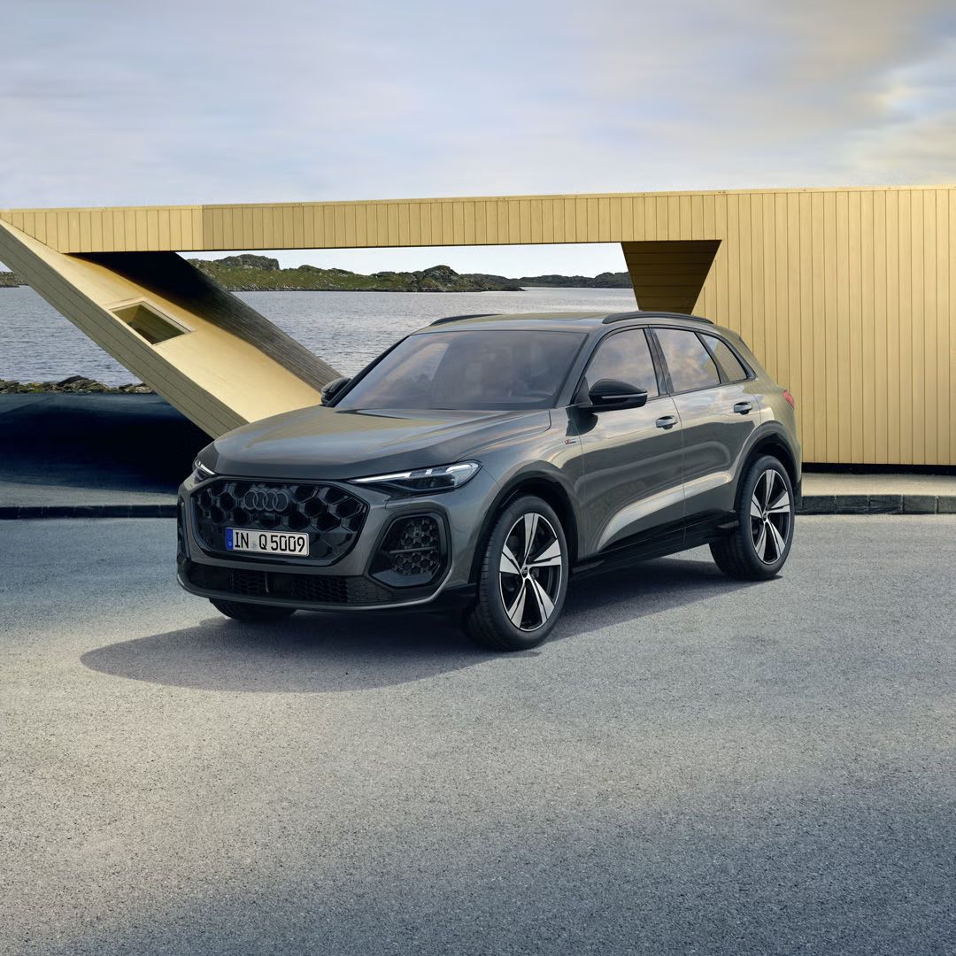 Der Q5 SUV in der edition one mit Kontrasten in Mythosschwarz steht im seitlichen Frontprofil auf einem Parkplatz direkt an der Küste. Dahinter ein futuristisches Haus.