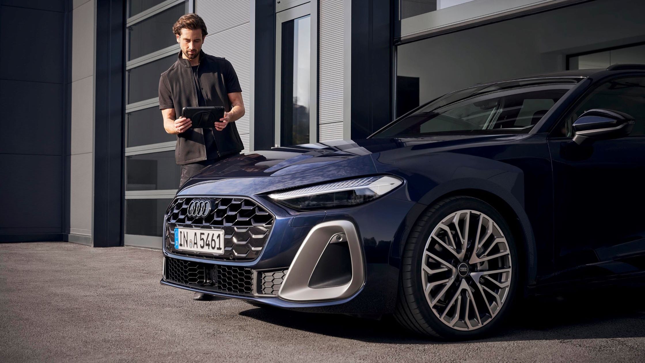 Ein Audi Service Techniker steht vor einem Audi und blickt auf sein Tablet