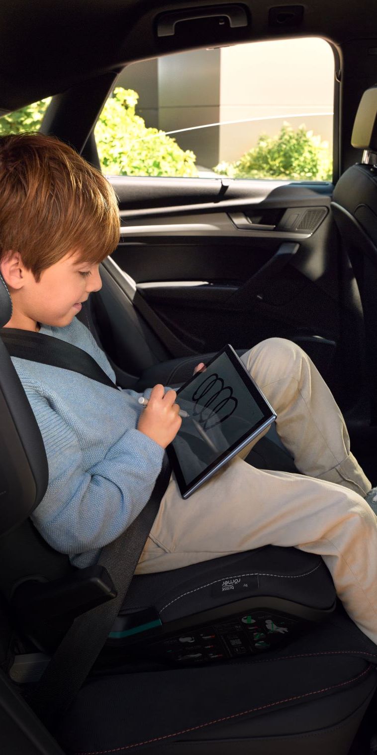 Ein Junge im Kindersitz spielt auf einem Tablet auf dem Rücksitz eines Audi.