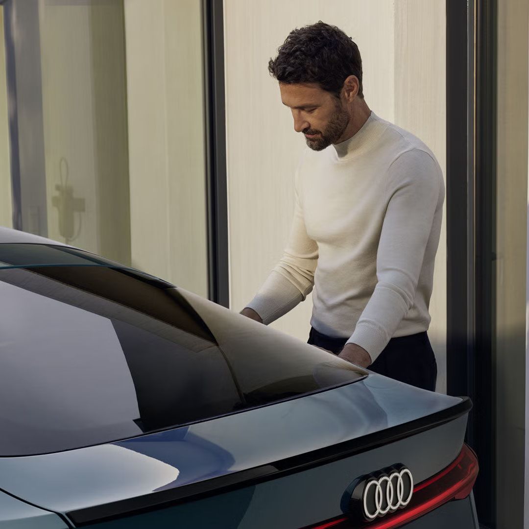 Ein junger Mann steht am Heck des S6 Sportback e-tron und schließt das Fahrzeug an eine Ladestation, die an der Wand montiert ist, an.