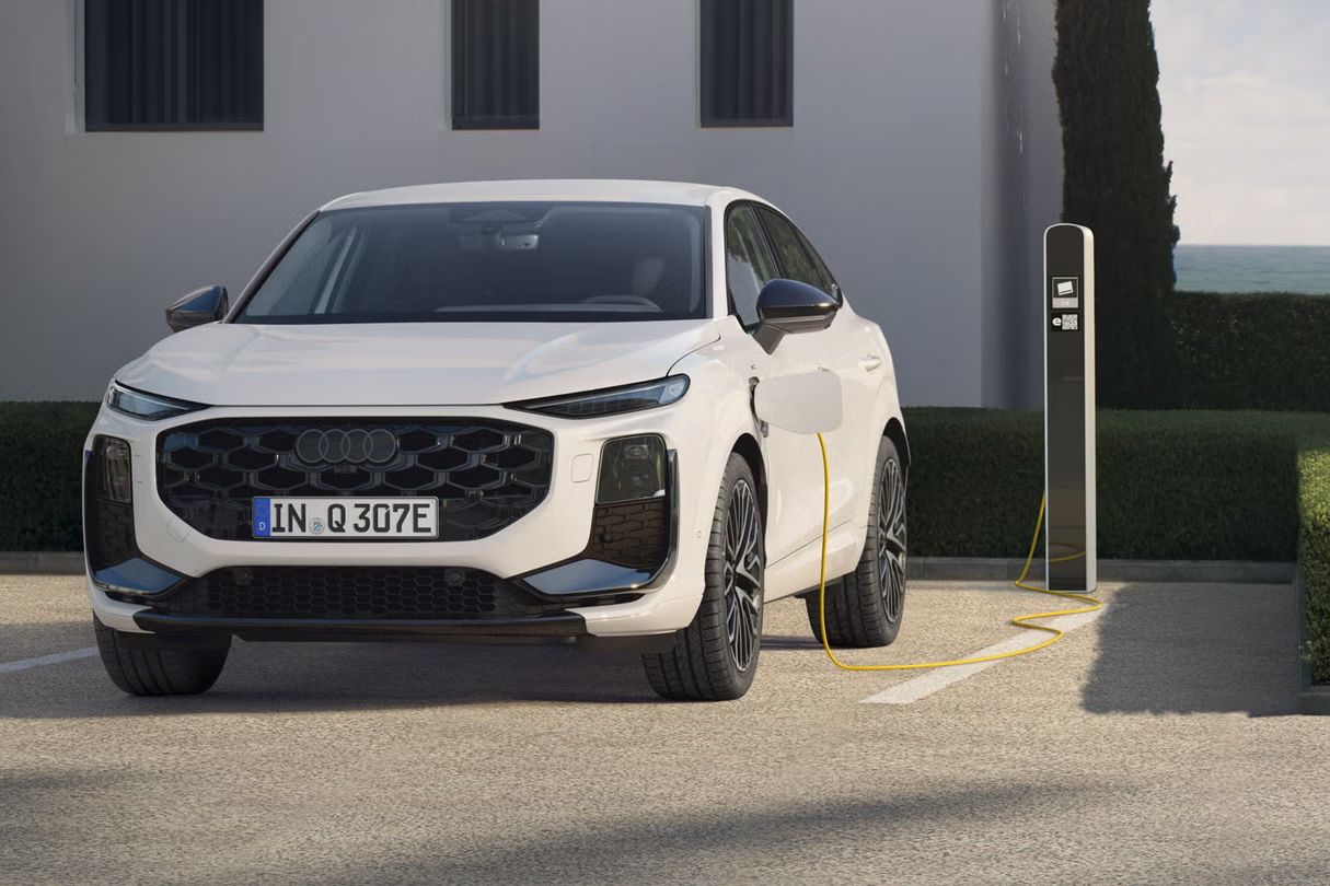 Ein weißer Q3 Sportback e-hybrid, vor einem modernen Haus parkend, lädt Strom an einer öffentlichen Ladesäule.	