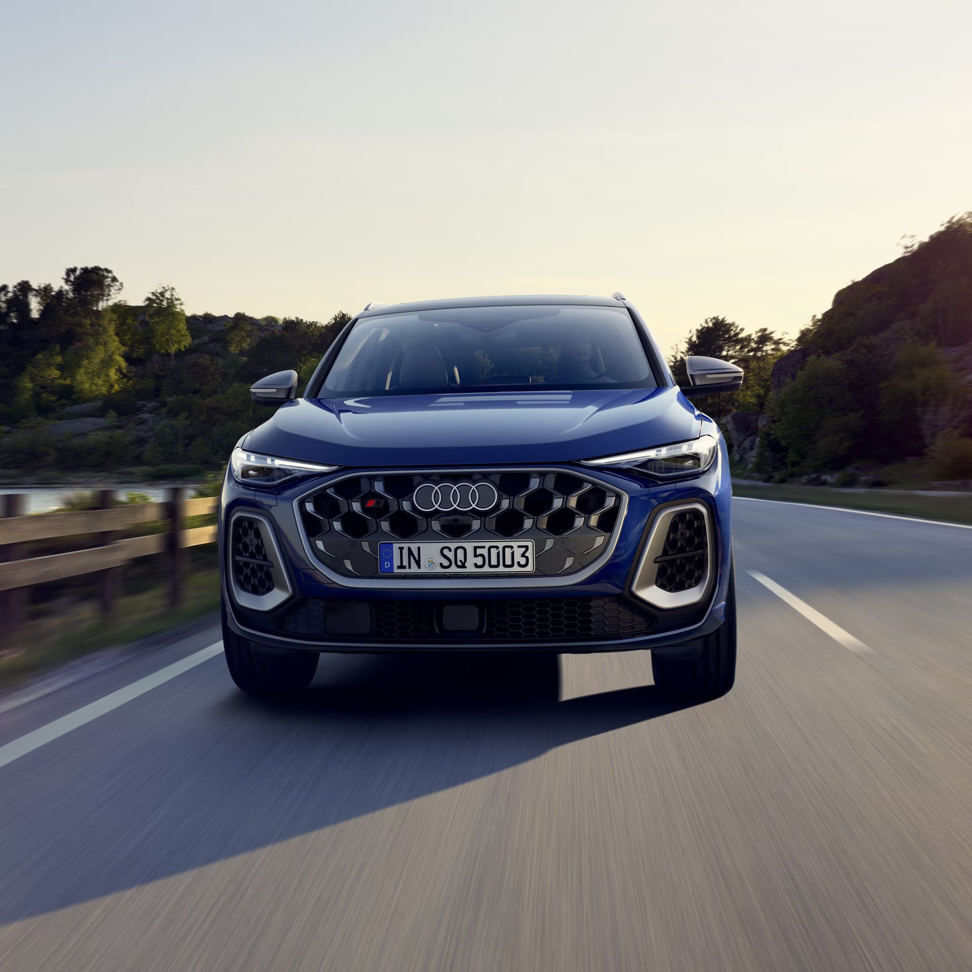 Frontprofil des SQ5 SUV in dunkelblau, welcher auf einer Straße durch die Natur fährt. Am Steuer sitzt eine junge Frau. 