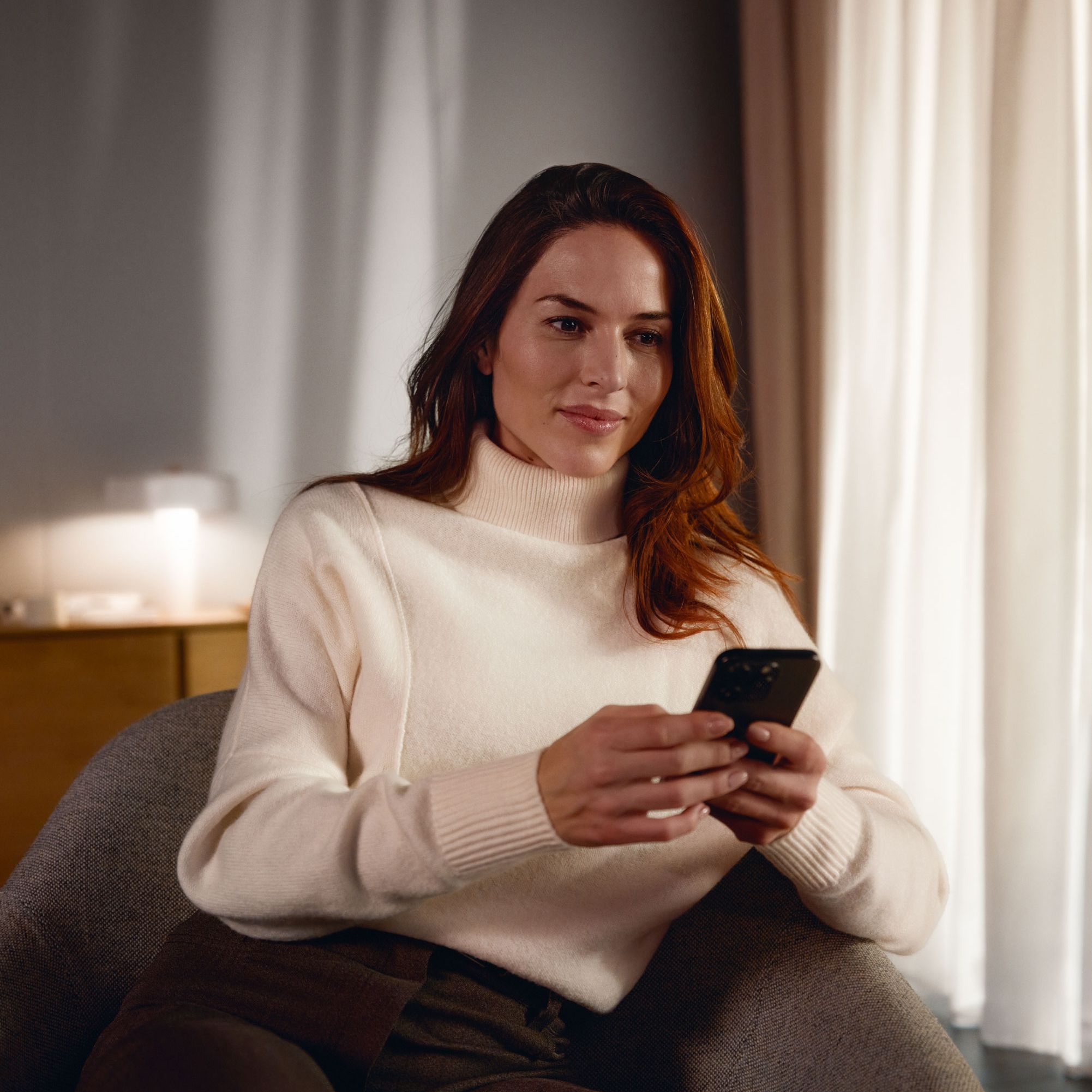 Eine Frau sitzt entspannt in einem Sessel und hält ein Smartphone in beiden Händen. 